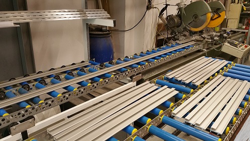 Bild der Zuschnittanlage für Aluminiumprofile mit einigen Profilen auf blauen Rollbahnen.